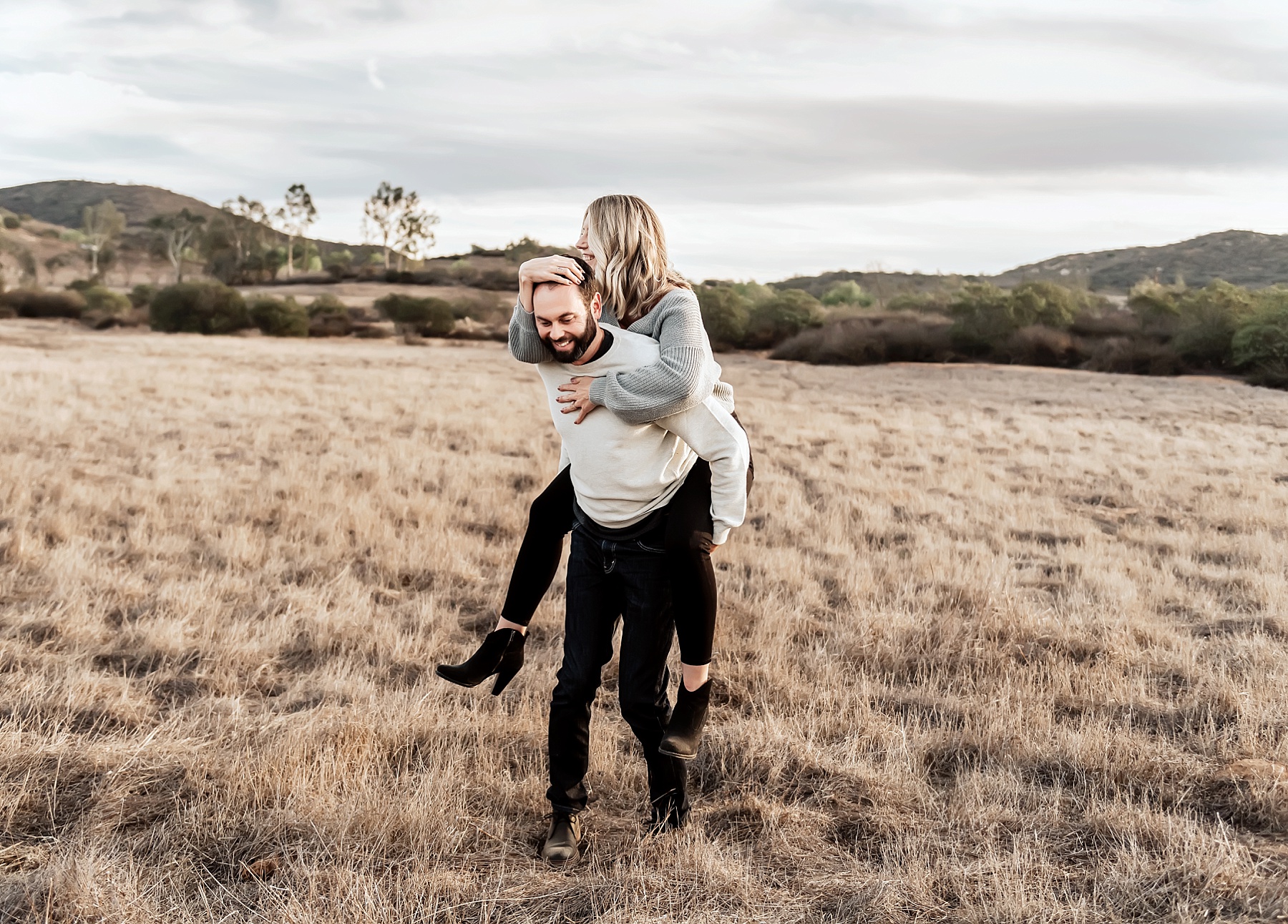 san diego family photographer couple pose piggy back ride in field
